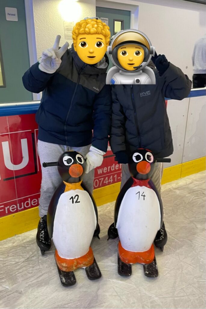 Eislaufen, zwei gungs stehen nebeneinander auf dem Eis. Zur Unterstützung stehen 2 Pinguine vor ihnen.